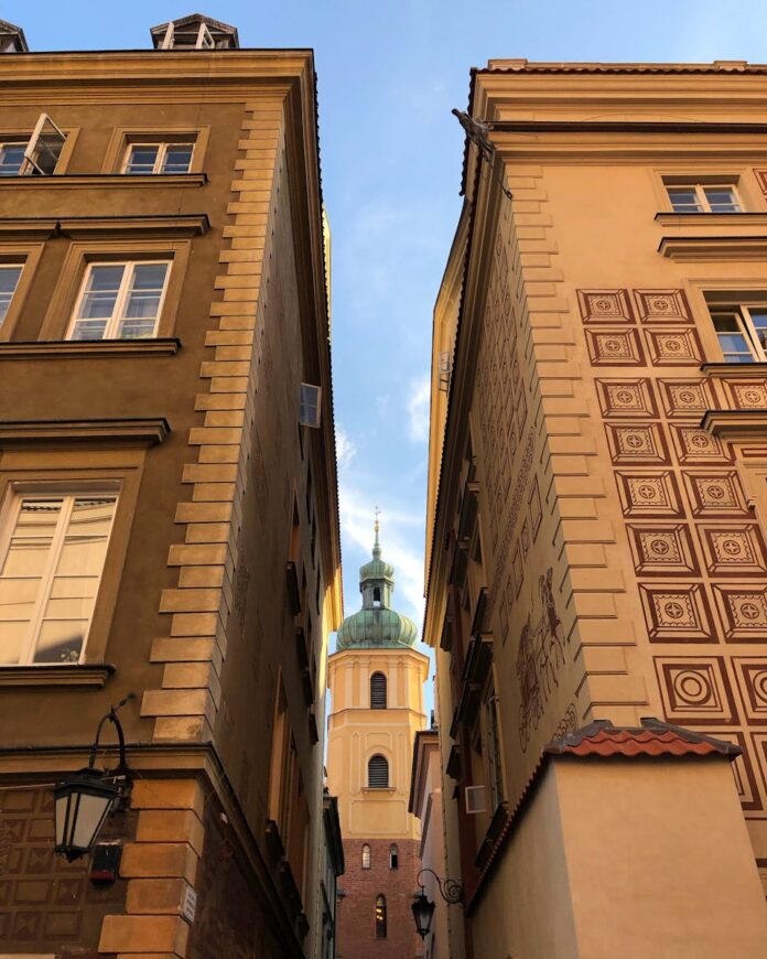 Charming view of a Warsaw church framed by historic old town buildings under a blue sky.